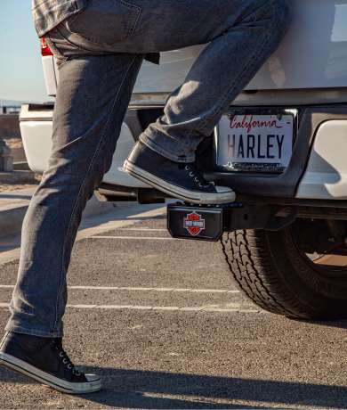 Person stepping onto a truck with a license plate that says "Harley" above a Harley Davidson Sticker