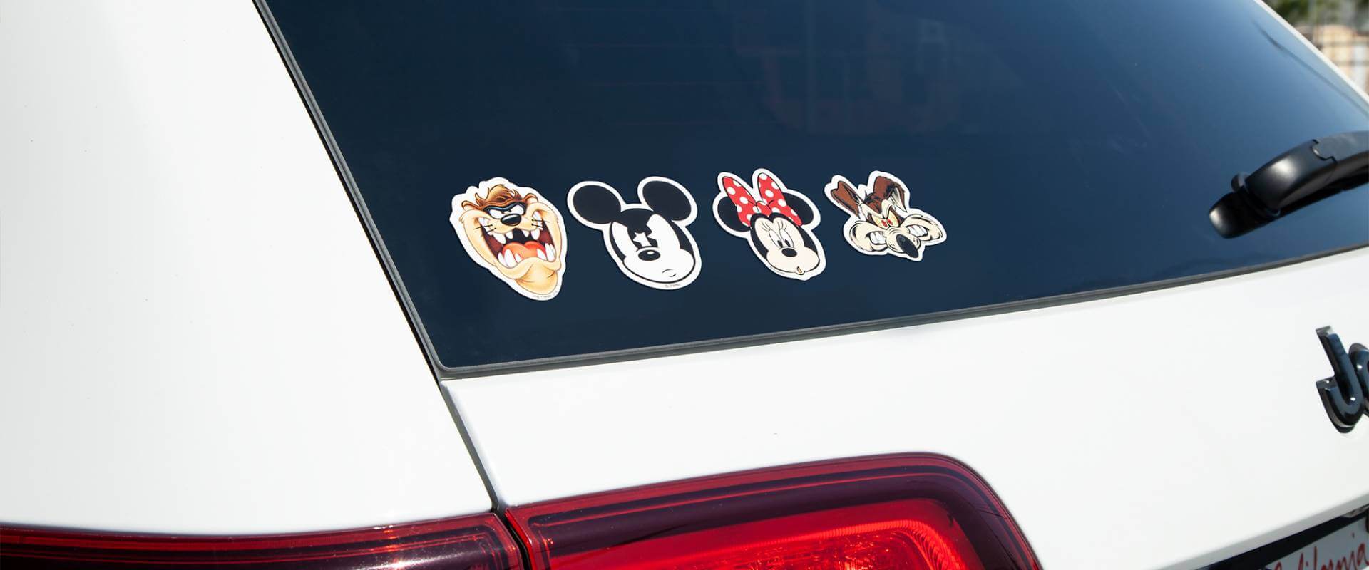 Stickers featuring cartoon characters from Disney and the Looney Toons on the rear window of a car.