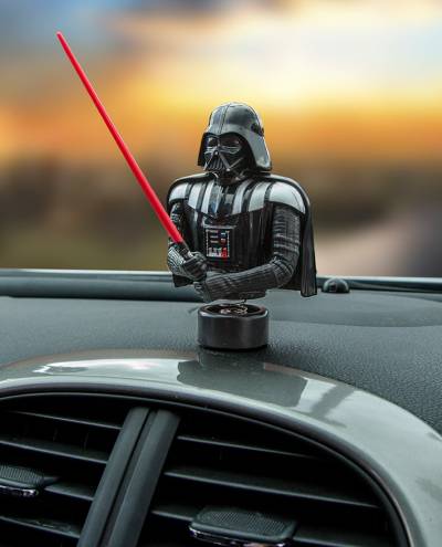 An auto ornament featuring the character Darth Vader from Star Wars on a car dashboard